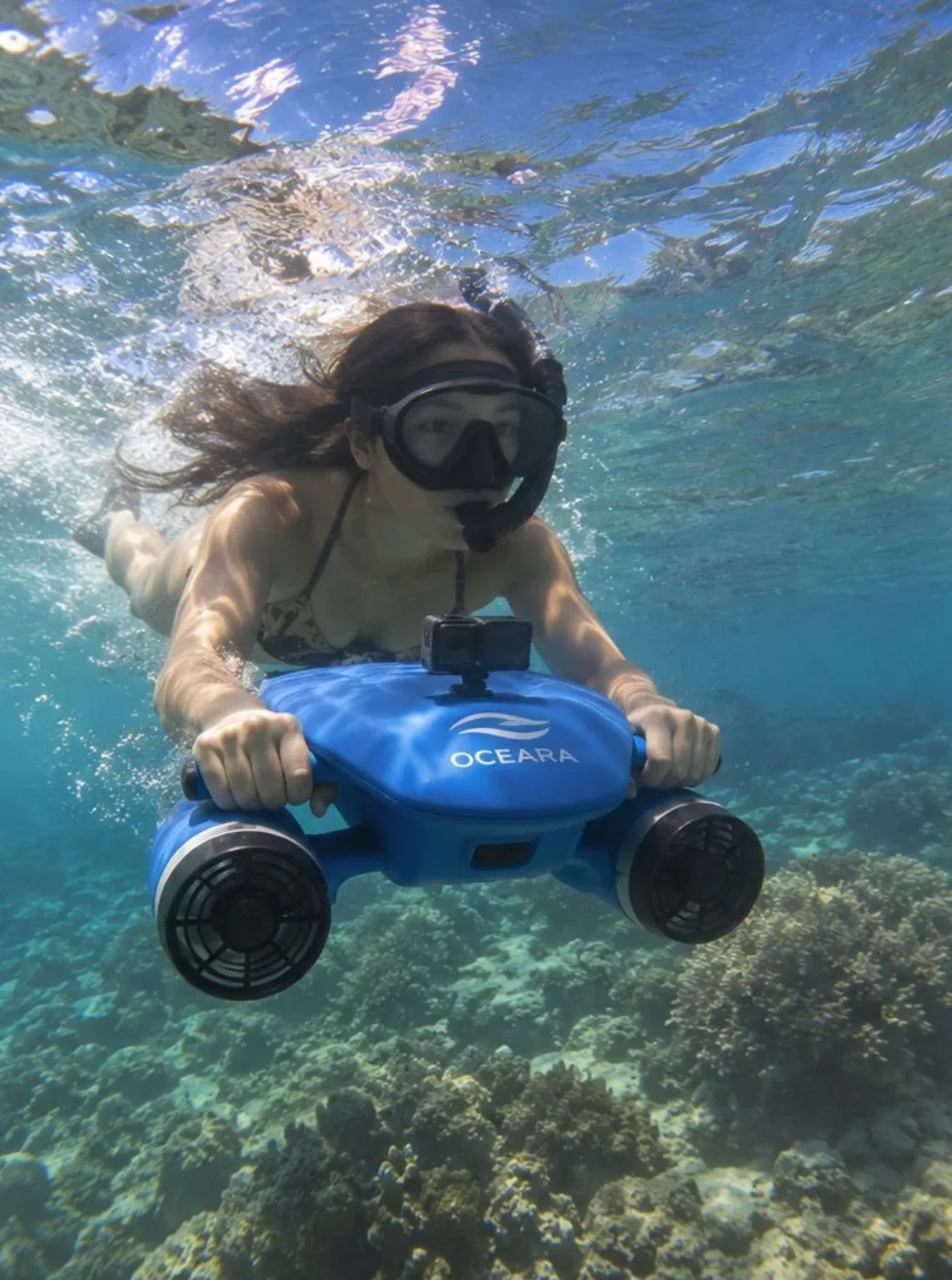 A snorkeller riding an OCEARA scooter over a coral reef